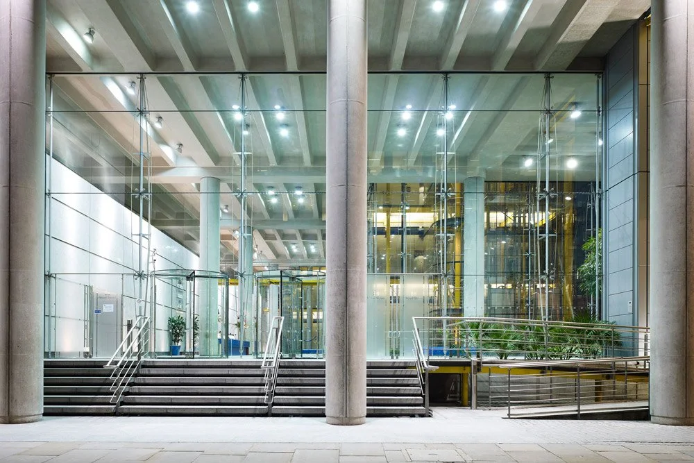 Modern building lobby with glass walls, metal railings, and steps leading up to an entrance.