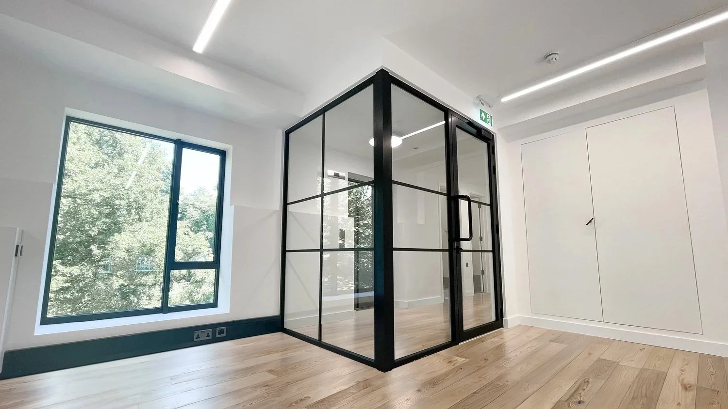 Modern interior room with large windows, wooden floor, and a glass cube structure with black metal frame.