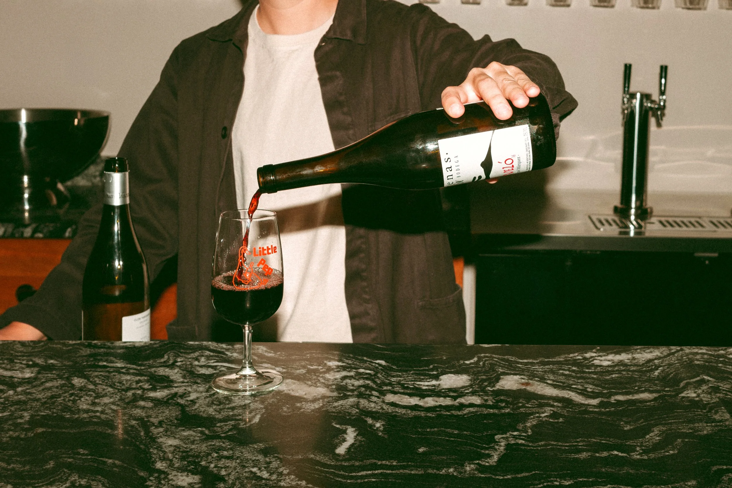 Person pouring red wine into a glass on a dark marble countertop.