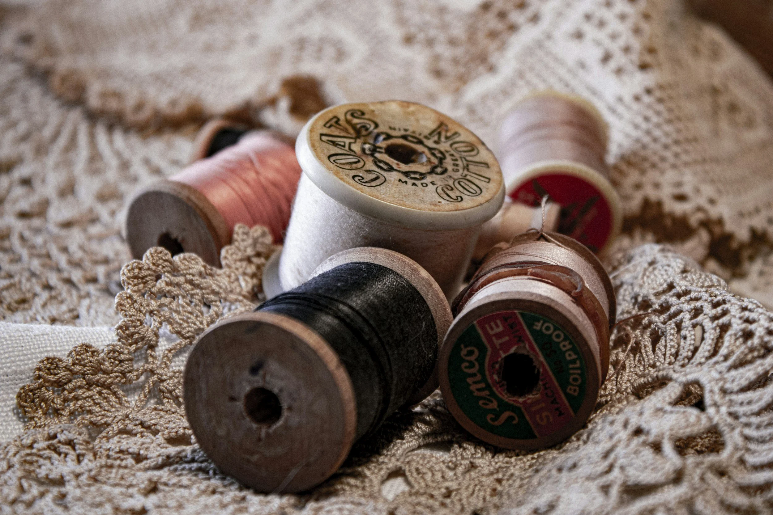 Several vintage wooden spools of thread lying on a lace fabric surface.