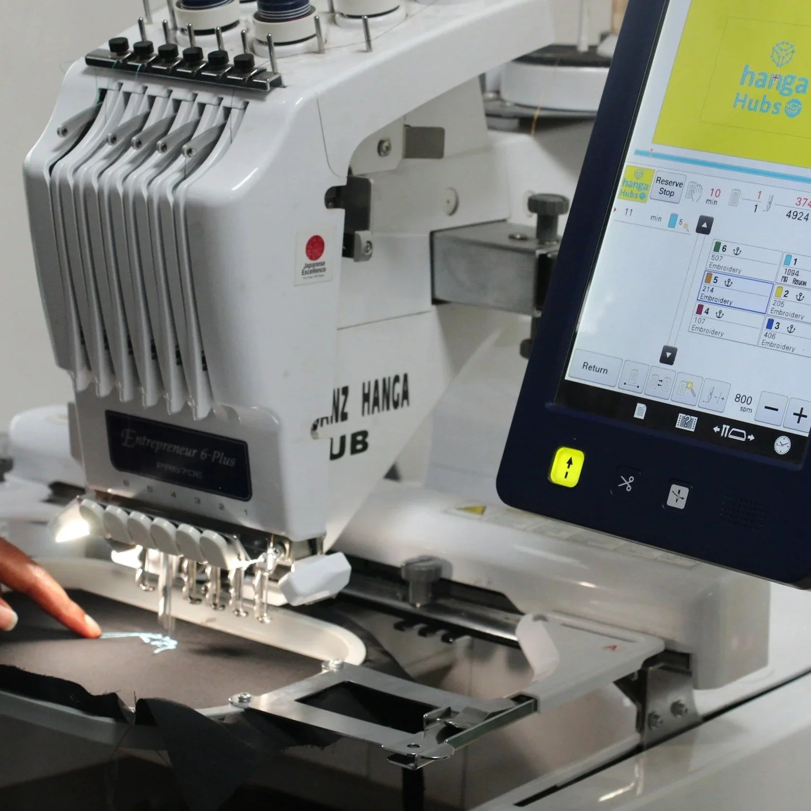 Close-up of a computerized embroidery machine with multiple embroidery heads and a touchscreen control panel.