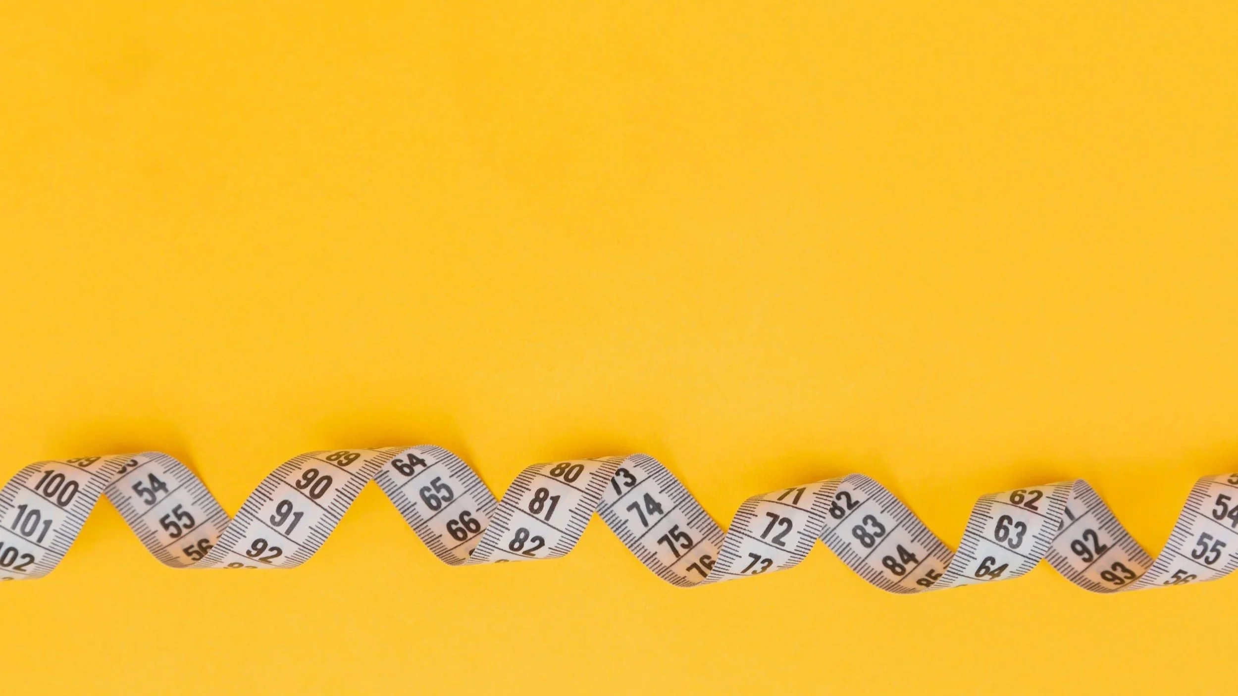 Several white measuring tapes with black numbers are arranged in a twisting line on a yellow background.