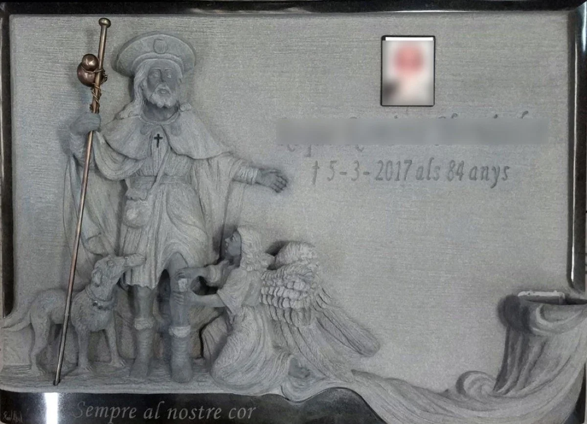Lápida esculpida artesanalmente en granito negro con un sofisticado juego de acabados que combina un marco perimetral pulido con el fondo en mate. La obra está protagonizada por una delicada escultura en relieve de San Roque acompañado por un ángel y