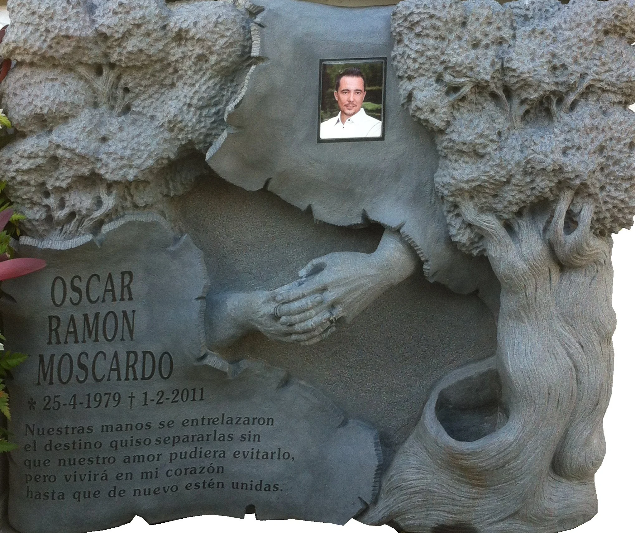 Lápida de profunda carga emocional esculpida artesanalmente en granito negro con acabado íntegramente mate. La obra está protagonizada por un conmovedor relieve de las manos del matrimonio entrelazadas junto a una olivera tallada, cuyo tronco se inte