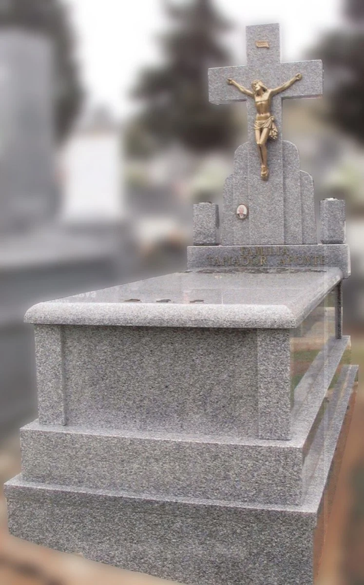 Panteón monumental esculpido en elegante granito gris Quintana, caracterizado por su diseño de volúmenes con diferentes grosores y una tapa superior de acabados limpios con cantos romos. La estructura se eleva coronada por un majestuoso cabezal en fo