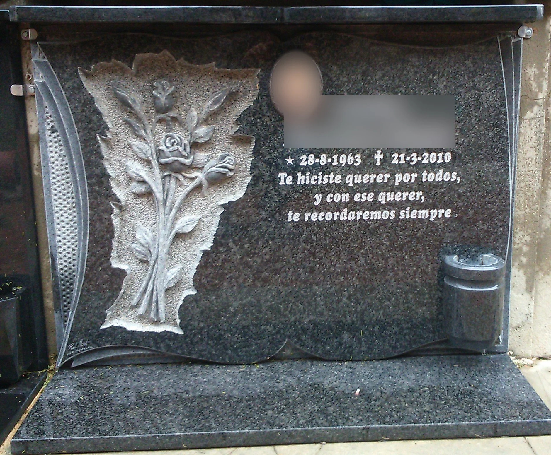 Escultura y lápida talladas en noble granito gris Sudáfrica, adornadas con un delicado ramaje floral en relieve, inscripción personalizada y medallón fotográfico. El conjunto se completa con una elegante repisa, cornisa y un búcaro integrado, rematad
