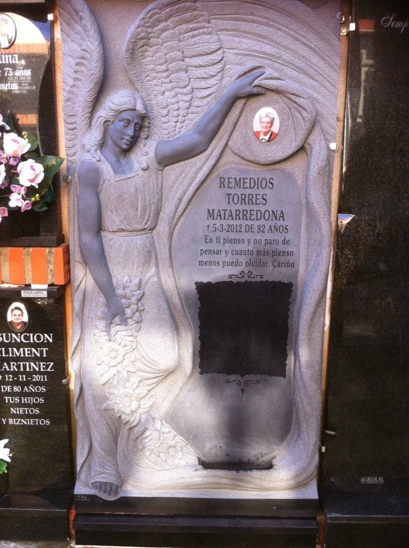 Lápida doble esculpida artesanalmente en granito verde, presidida por la delicada escultura en alto relieve de un ángel que sostiene el manto donde se ubica la fotografía y la inscripción. La obra destaca por un magistral contraste de texturas y acab
