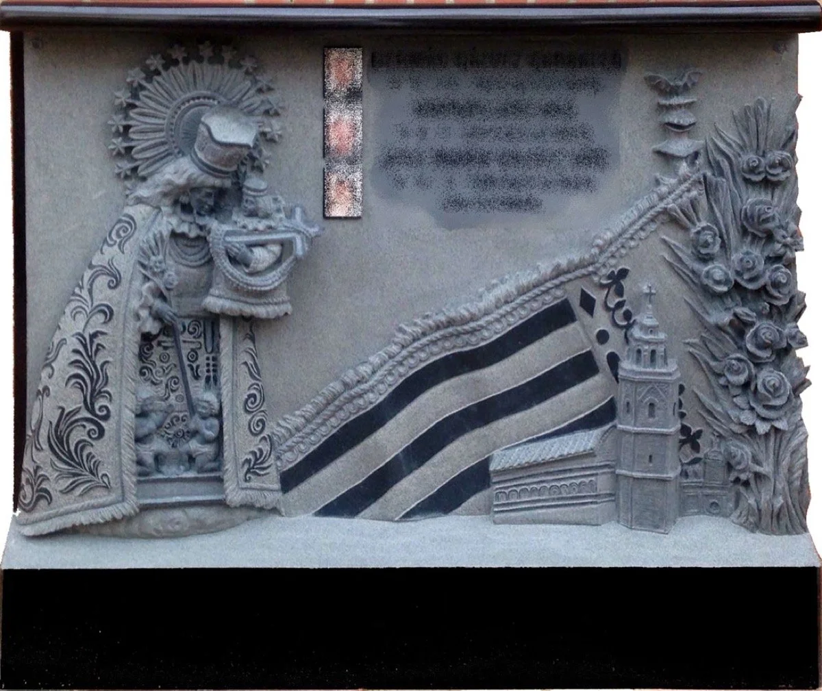 Impresionante lápida doble esculpida en granito negro, una obra de altísima complejidad y significado que rinde homenaje a los vínculos más íntimos de la familia. La composición está presidida por la Virgen de los Desamparados con el detalle de su ve