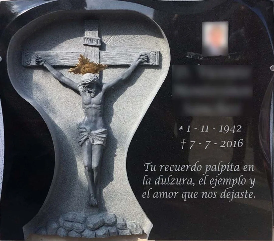 Lápida esculpida artesanalmente en granito negro, protagonizada por el relieve de un Cristo en la cruz y enmarcada por un contorno de silueta totalmente personalizada, diseñada a medida para la familia. La composición se completa con una elegante ins