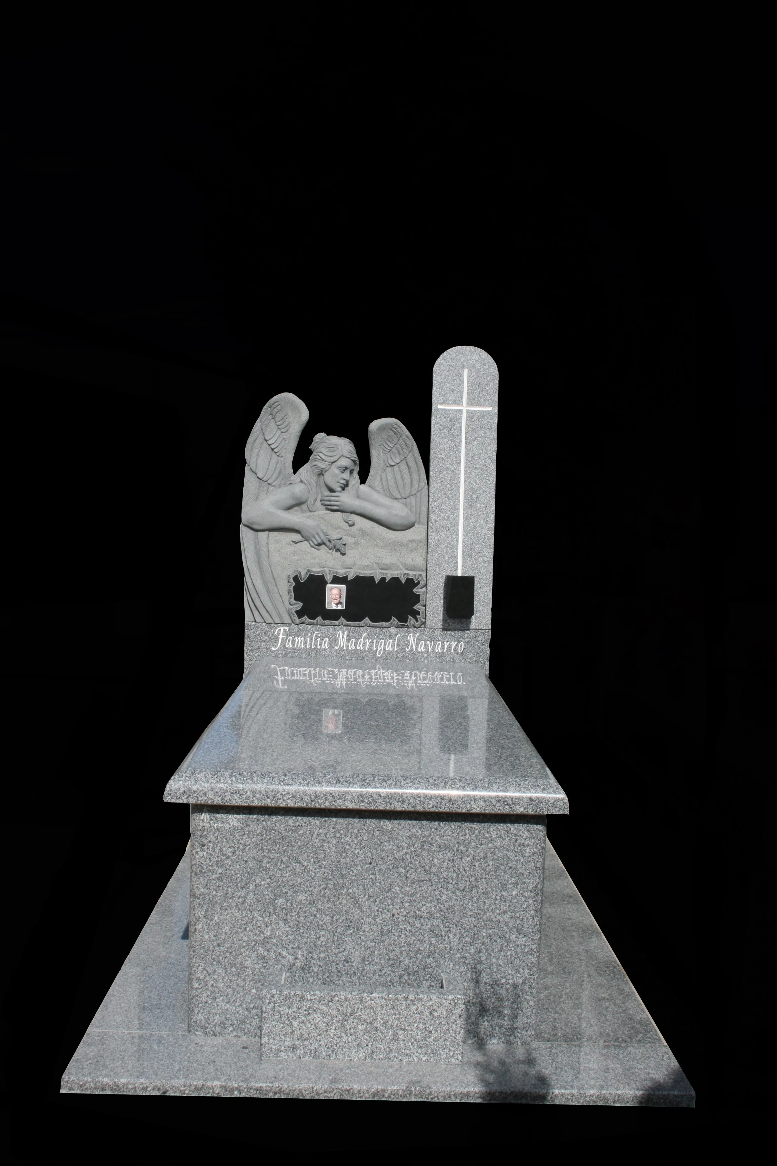 Impresionante panteón en granito gris Quintana con un perímetro estructurado en diferentes grosores de piedra que enmarca el conjunto con gran solidez. El frontal destaca por una magnífica escultura de un ángel cuyas alas abrazan y protegen la zona d
