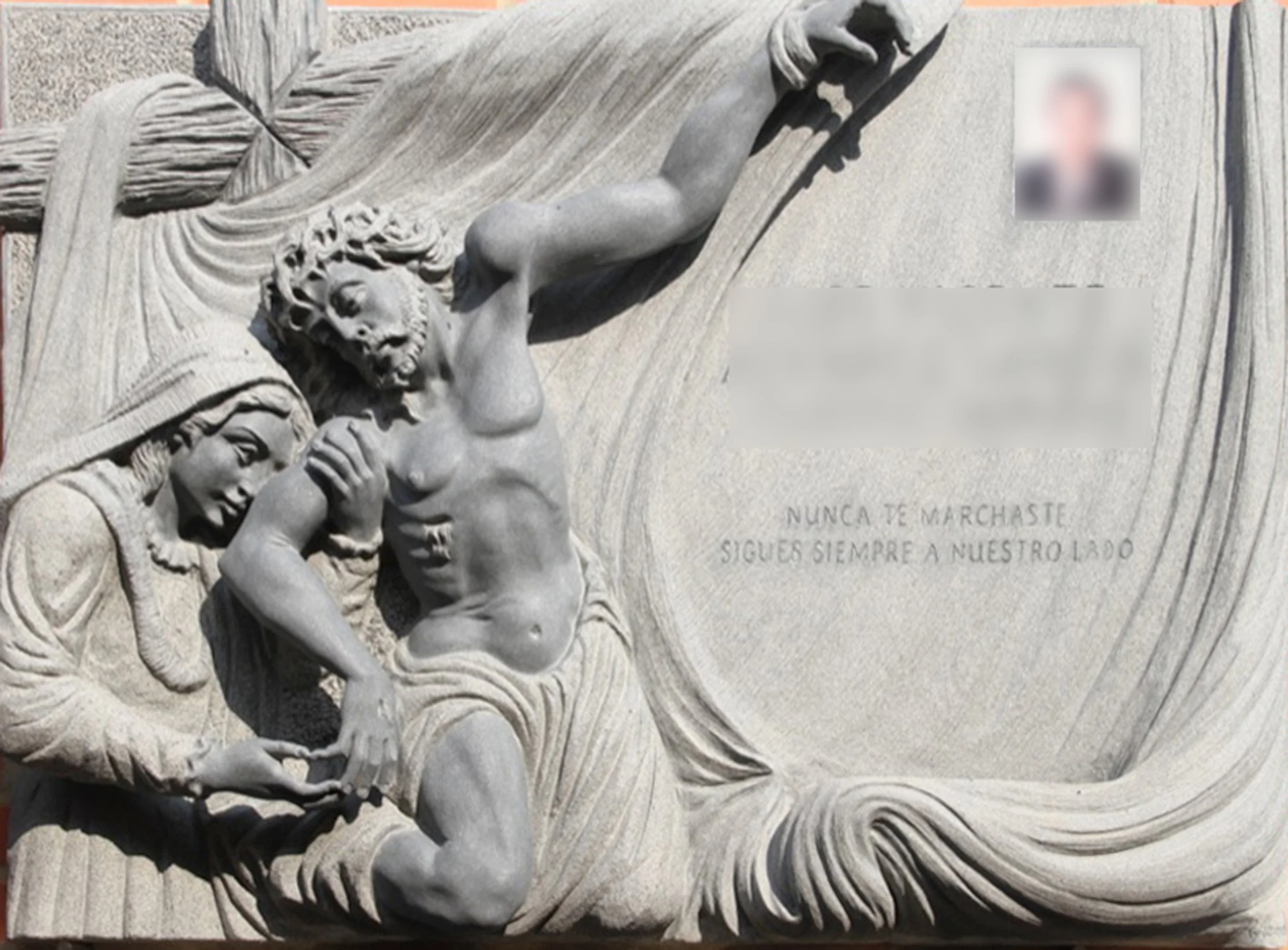 Lápida esculpida a mano en granito negro, protagonizada por las figuras de Jesús, la Virgen y la cruz talladas en relieve sobre un fondo completamente rebajado, y enmarcada por delicados adornos de cortina que envuelven la escena. La composición se c