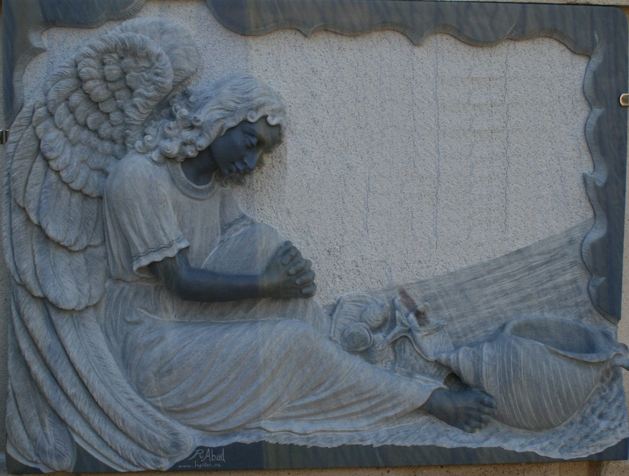 Lápida esculpida en exclusivo granito azul Macahuba —un material de excepcional dureza y hermosos tonos azulados—, protagonizada por un espectacular ángel tallado en relieve con fondo rebajado. Destaca por el contraste de sus acabados, con las carnes