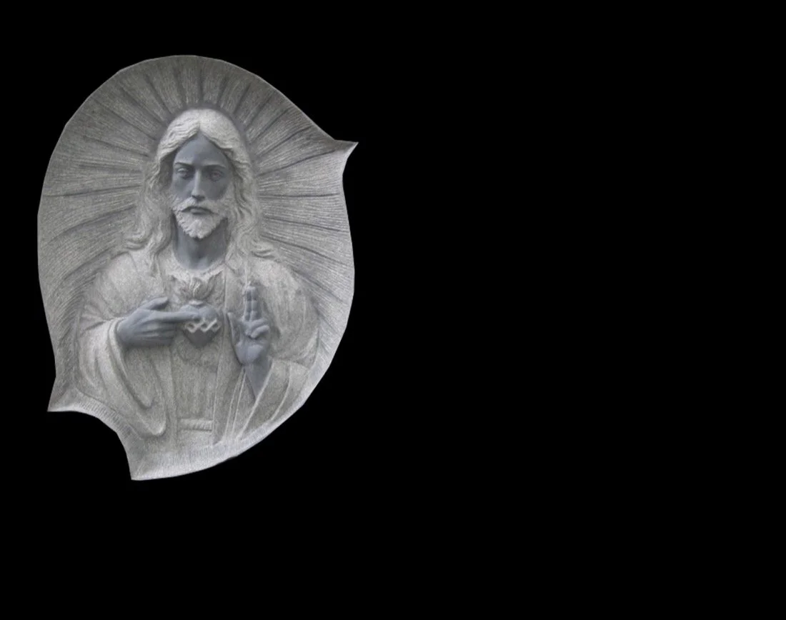 Lápida de granito negro con escultura en relieve del Sagrado Corazón de Jesús de medio cuerpo. Obra tallada a mano por el escultor Raúl Abad en nuestro taller de Alfara del Patriarca (Valencia).
