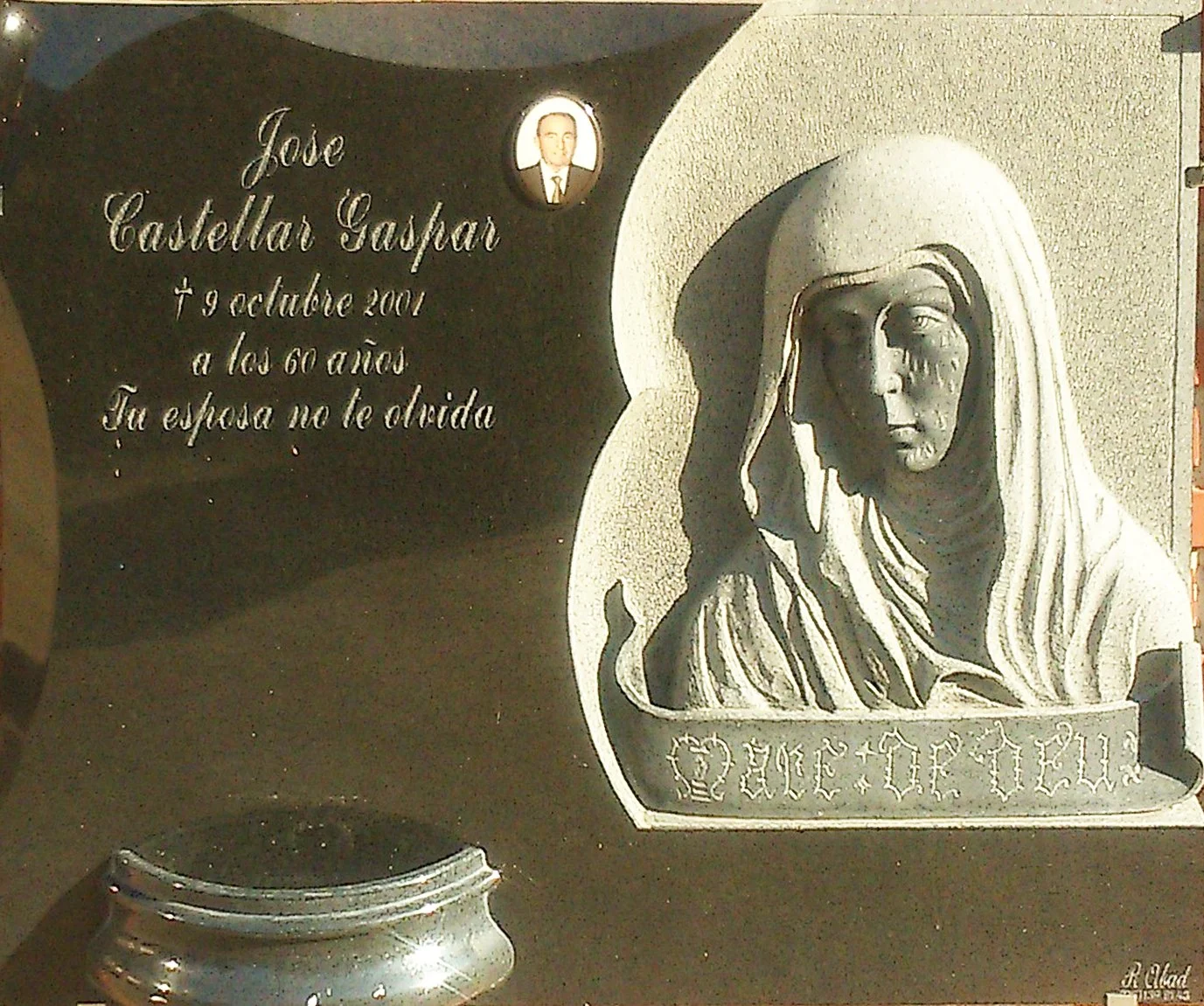 Lápida en elegante granito negro con una delicada escultura de la Virgen tallada a mano en el lateral derecho. El diseño se completa con finos biseles perimetrales y una jardinera integrada. Obra de arte funerario totalmente personalizada y elaborada