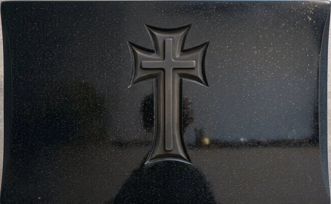 Lápida doble en granito negro con fondo pulido y un fino tallado en relieve que da forma a una cruz personalizada. Una elegante pieza de diseño sobrio y distinguido de arte funerario, elaborada artesanalmente en nuestro taller de Alfara del Patriarca
