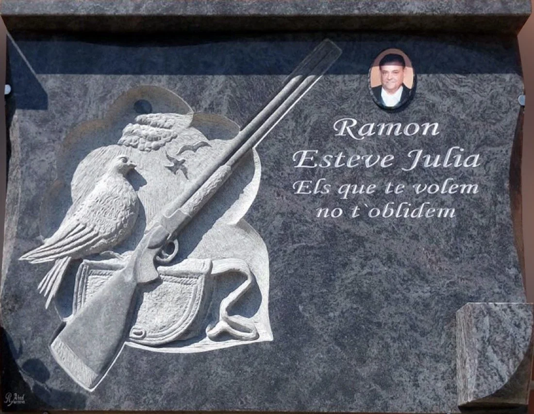 Lápida en granito azul Magnetic Blue con escultura personalizada de cazador que incluye escopeta, paloma y su alforja, acompañada de biseles, cornisa y búcaro sobrepuesto. Obra tallada a mano por el escultor Raúl Abad en nuestro taller de Alfara del 