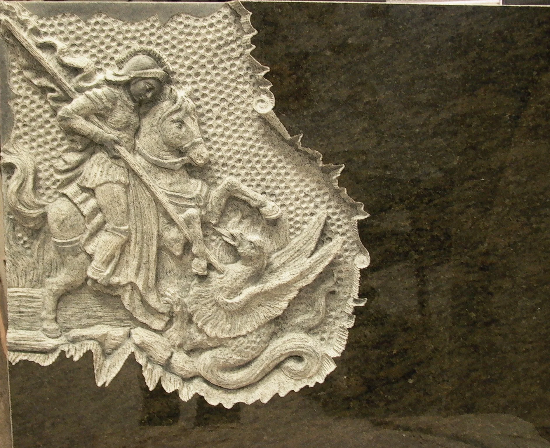 Lápida en exclusivo granito verde con una impresionante escultura de San Jorge tallada a mano con increíbles detalles. Una auténtica obra de arte funerario de máxima precisión y belleza, elaborada de forma artesanal en nuestro taller de Alfara del Pa