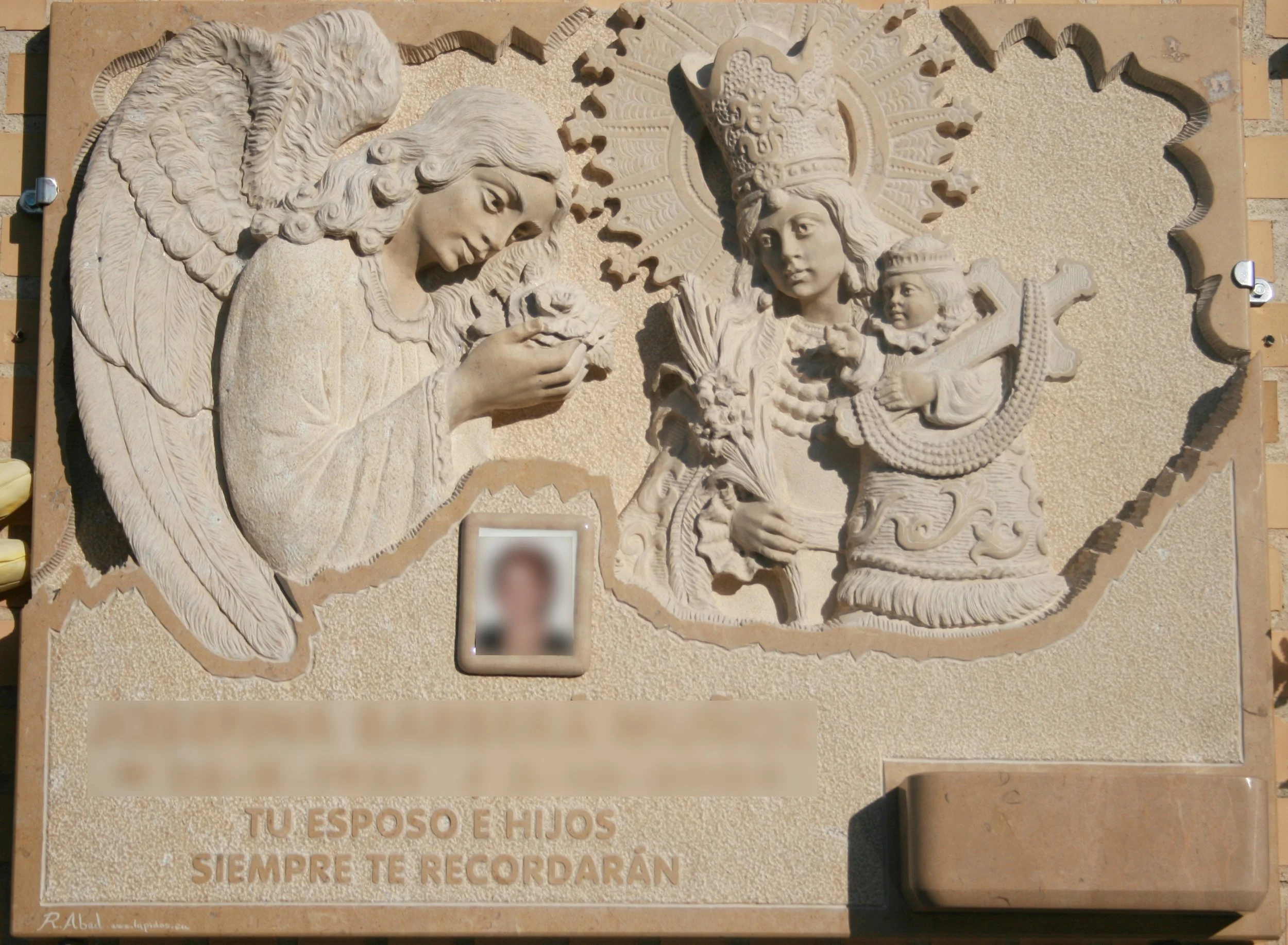 Lápida esculpida artesanalmente en mármol Cenia, protagonizada por las figuras de un ángel y la Virgen de los Desamparados con un extraordinario nivel de detalle, especialmente en los rasgos de la Virgen y las finas plumas de las alas. La composición