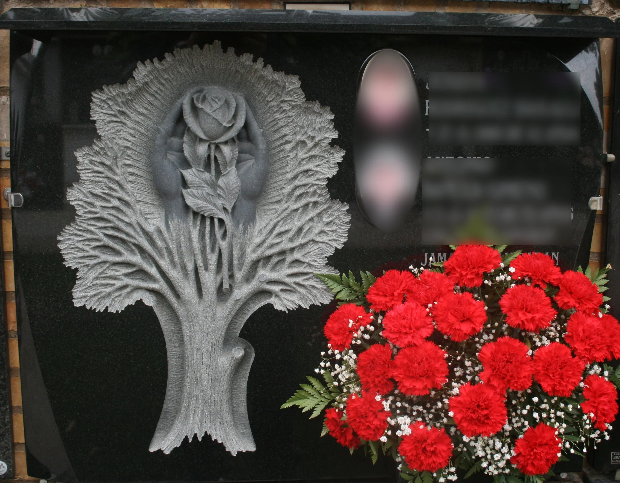 Lápida de elegante granito negro en la que destaca un delicado bajorrelieve escultórico: un árbol simbólico del que surge una mano sosteniendo con ternura una rosa. Una pieza cargada de emotividad y significado personal, esculpida de forma totalmente