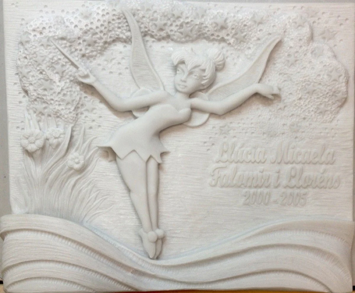Columbario esculpido artesanalmente en noble mármol blanco Macael, concebido como un tierno y emotivo homenaje a una niña de 5 años. La obra está protagonizada por su personaje favorito, Campanilla, rodeada de flores y árboles, e integrada de forma f