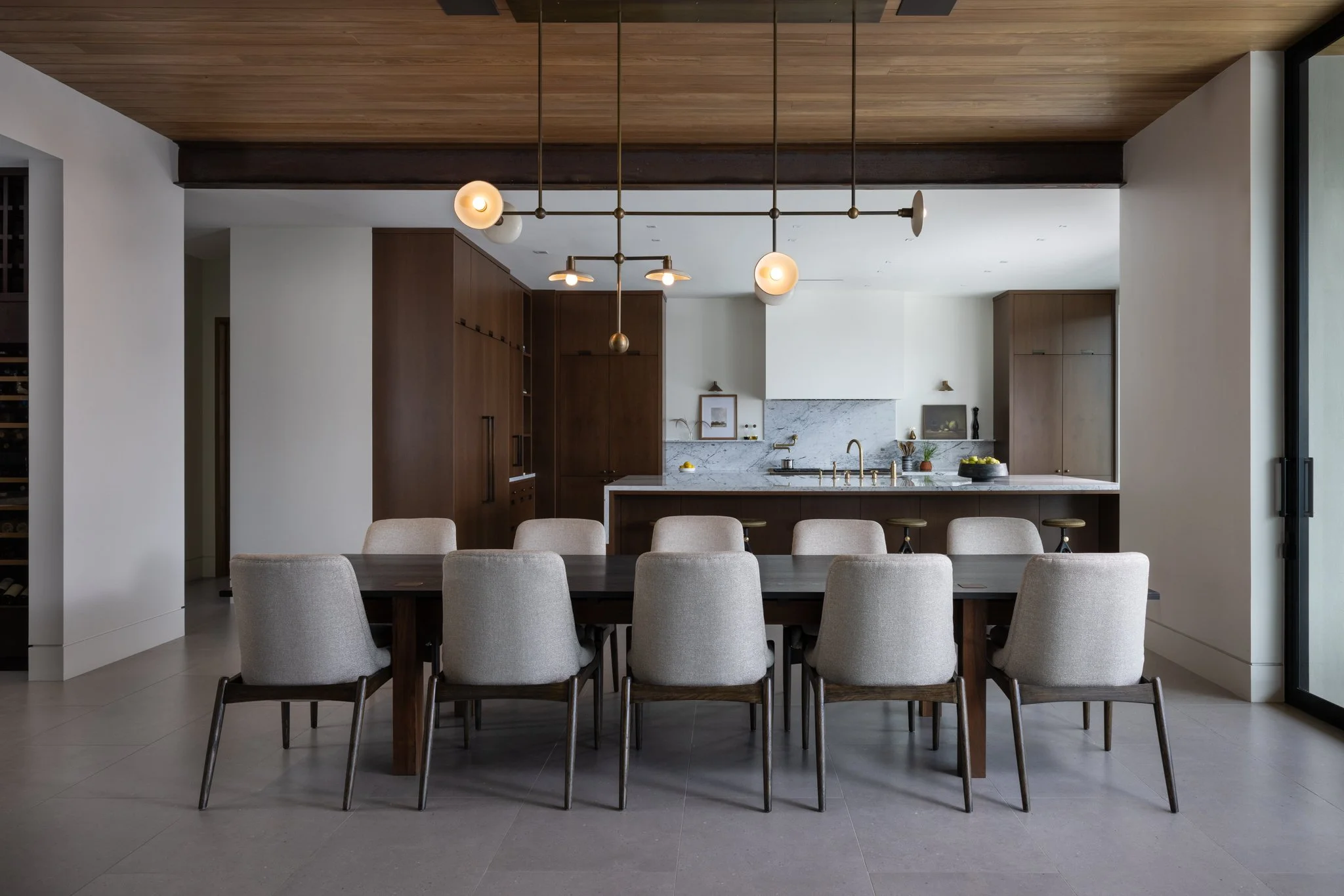Modern dining area with a custom made dark wood table by joe wolf of wolf wood co and four hands chairs, open-concept kitchen with marble countertops, custom oak cabinets, and custom linear pendant lighting fixture by buzzel studios.