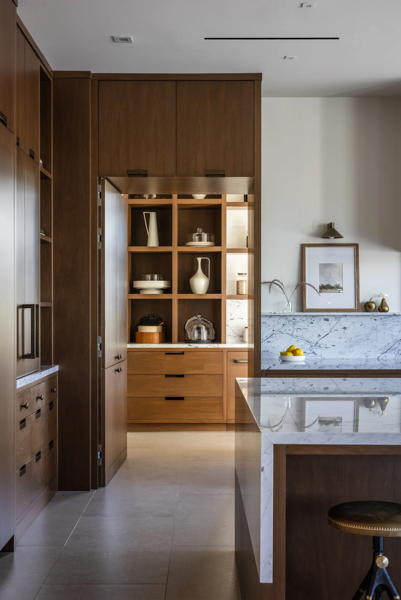 Modern kitchen with wooden cabinetry, open shelving with decorative items, marble countertop, and a framed picture on the wall.