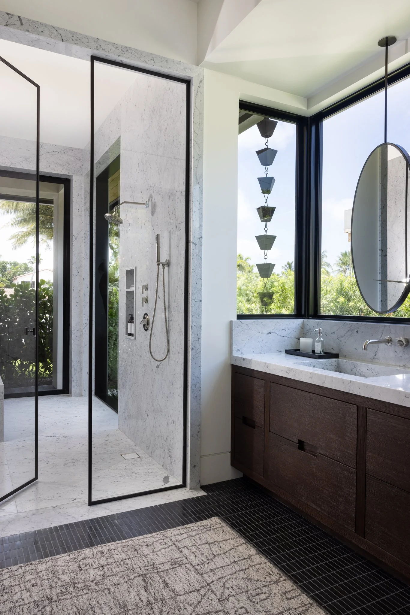 Modern bathroom with Opus Stone marble, large windows, and a walk-in shower with glass doors. Custom oak vanity with white marble counters and backsplash with large mirror, and waterworks wall mounted fixtures. Black mosaic tiles from Opus Stone. 