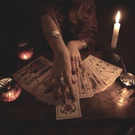 Person performing a tarot card reading with tarot cards, candles, and a dark background.