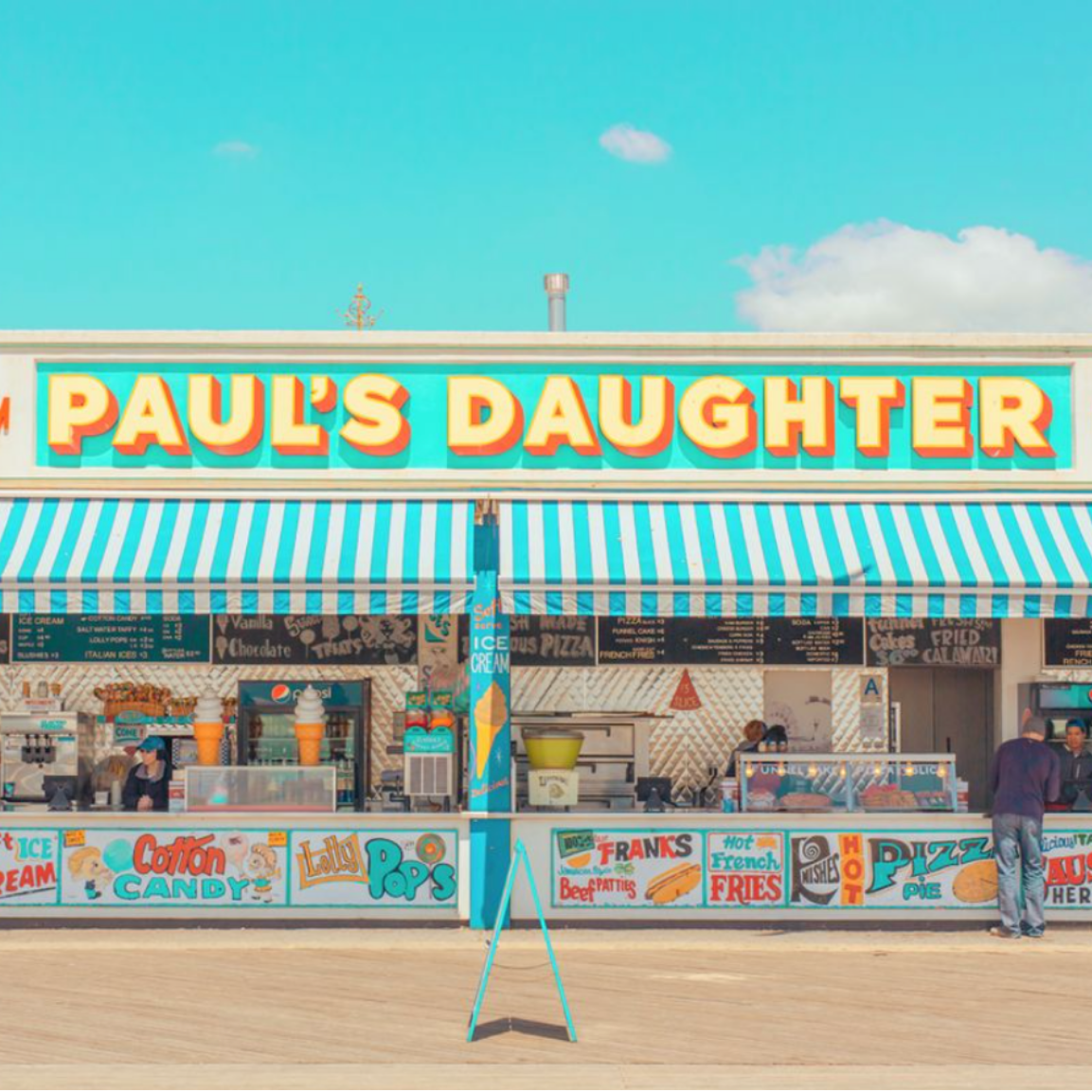 Colorful ice cream shop named 'Paul's Daughter' with a striped awning, serving ice cream, cotton candy, popcorn, pizza, fries, fried calamari, and other snacks on a sunny day.