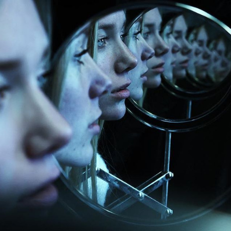 Multiple women looking into a mirror, with their faces reflected in the glass.