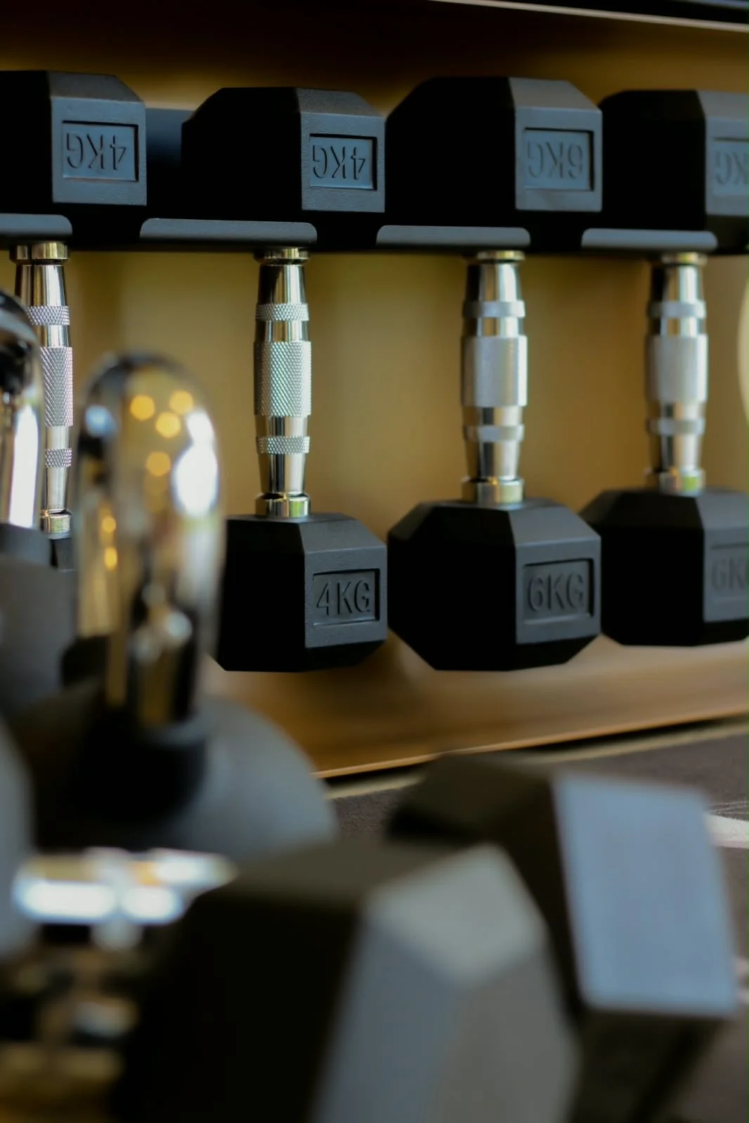 A row of black dumbbells with silver handles on a wooden rack, labeled with weights from 4kg to 6kg at Physio Goals clinic