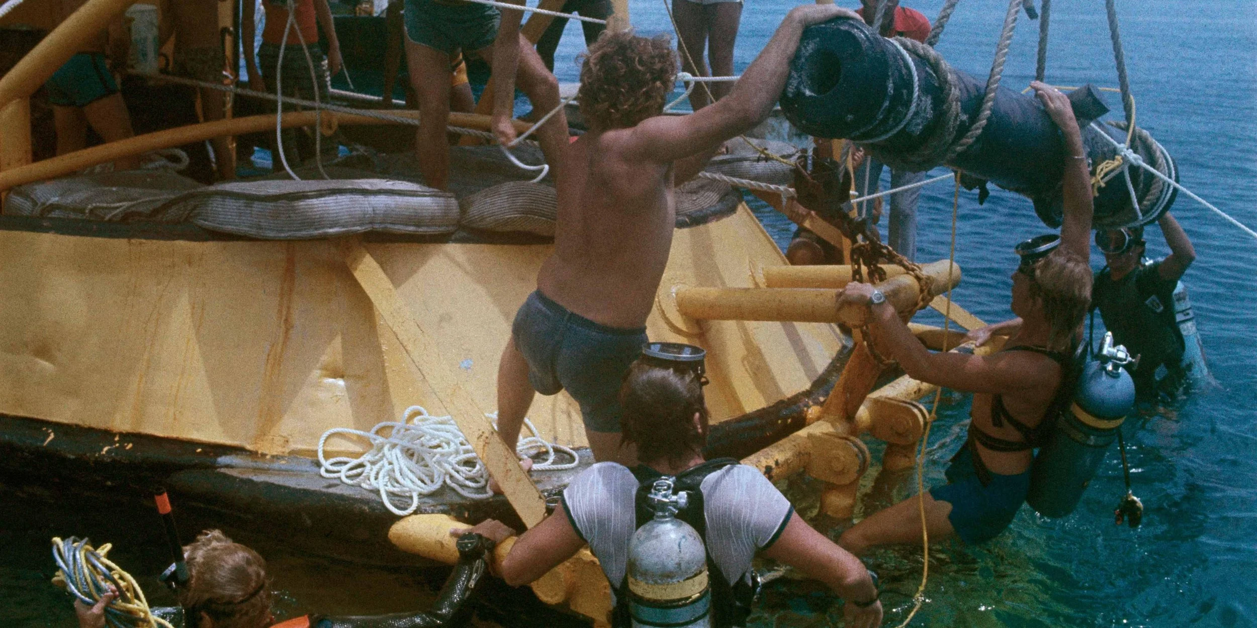 Multiple people are on a boat, with some hanging over the side, wearing snorkeling gear and life jackets, preparing for a diving adventure in the water.