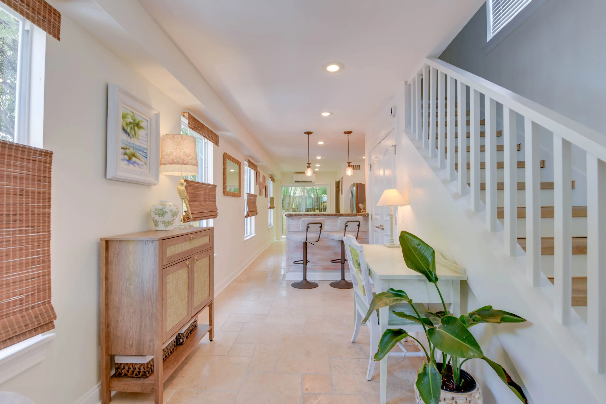 Interior view of a bright, modern home with a staircase, artwork on the walls, and dining area with pendant lights.