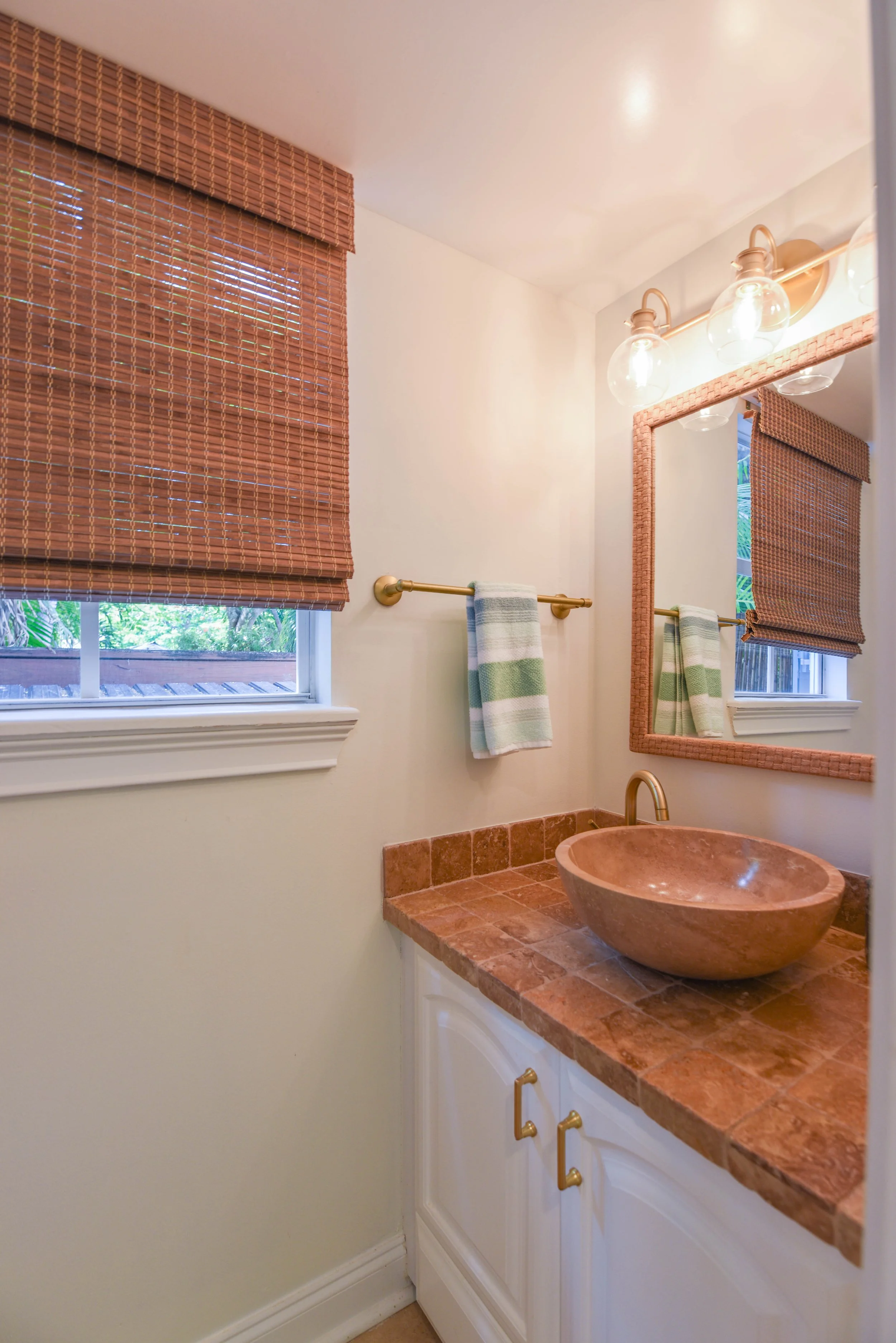 Bathroom with window blinds, a mirror, a sink bowl, and cabinet with gold handles.