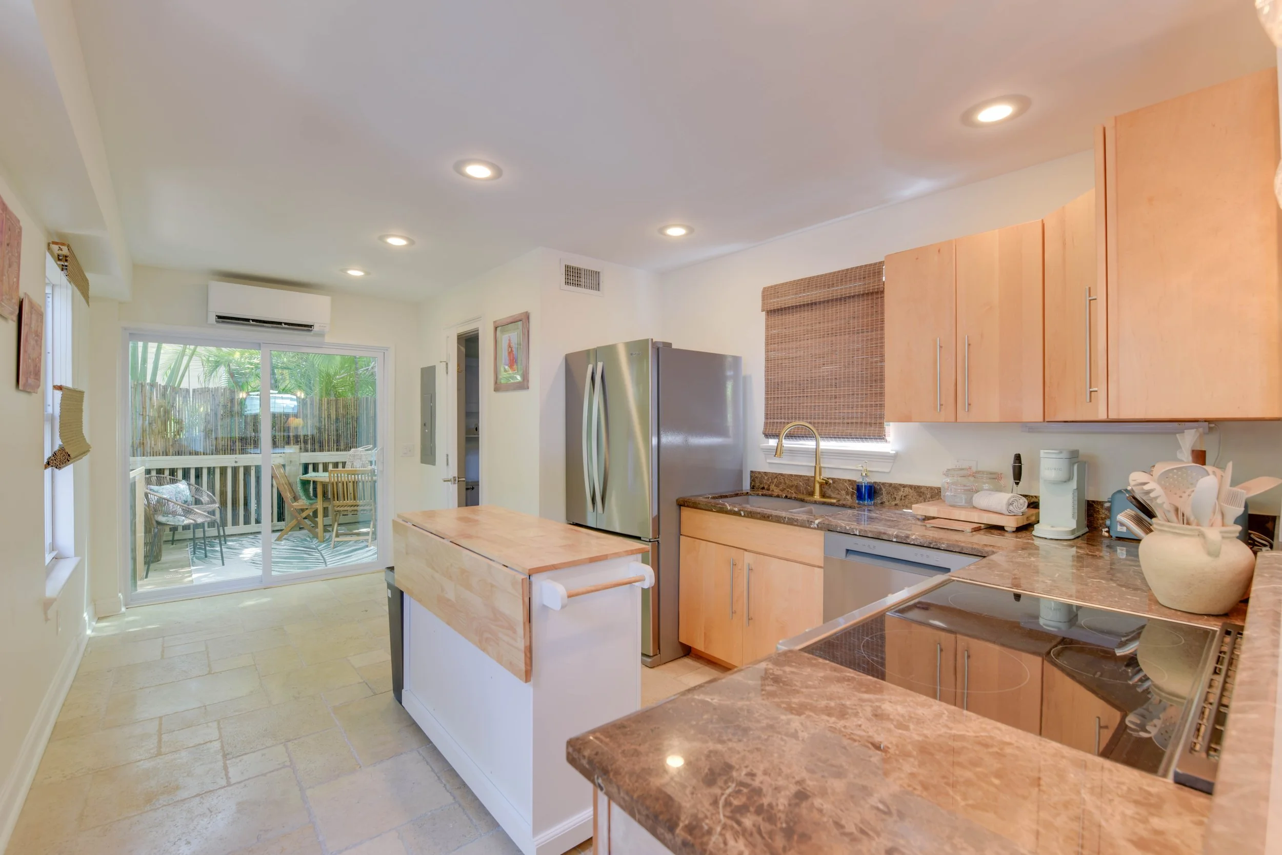 Kitchen with wooden cabinets, marble countertops, stainless steel refrigerator, and a sliding glass door leading to a patio with outdoor chairs.