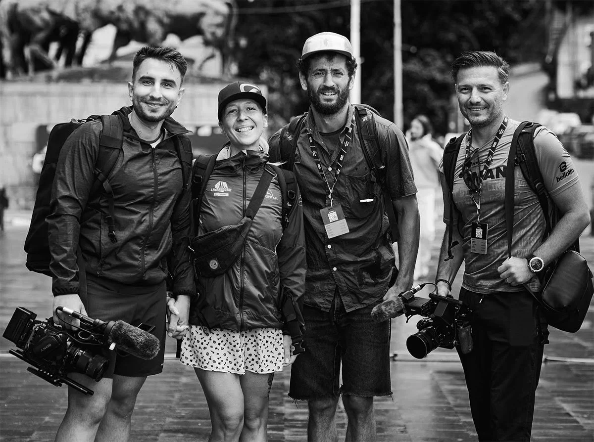Group of four smiling people with cameras and backpacks standing outdoors.