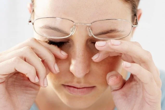 A person with glasses pinching the bridge of their nose, eyes closed, appearing to experience discomfort or pain.