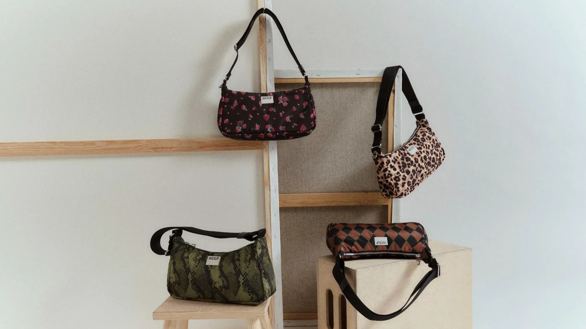 Four handbags hanging on a wooden and fabric display stand against a plain wall.