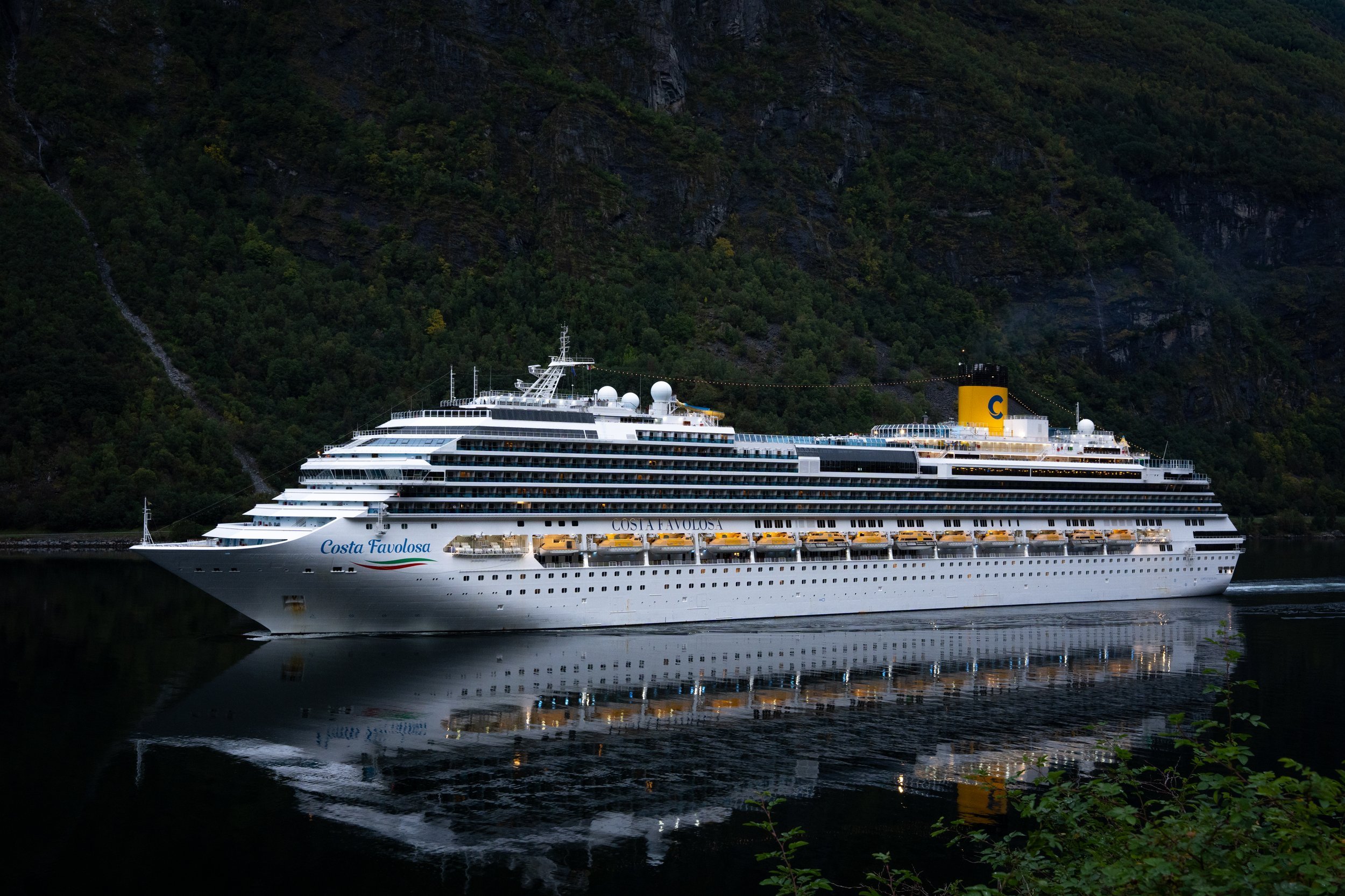 Kreuzfahrtschiff in einem norwegischen Fjord vor dunklen Felswänden – Fotografie von Leon Hartmann