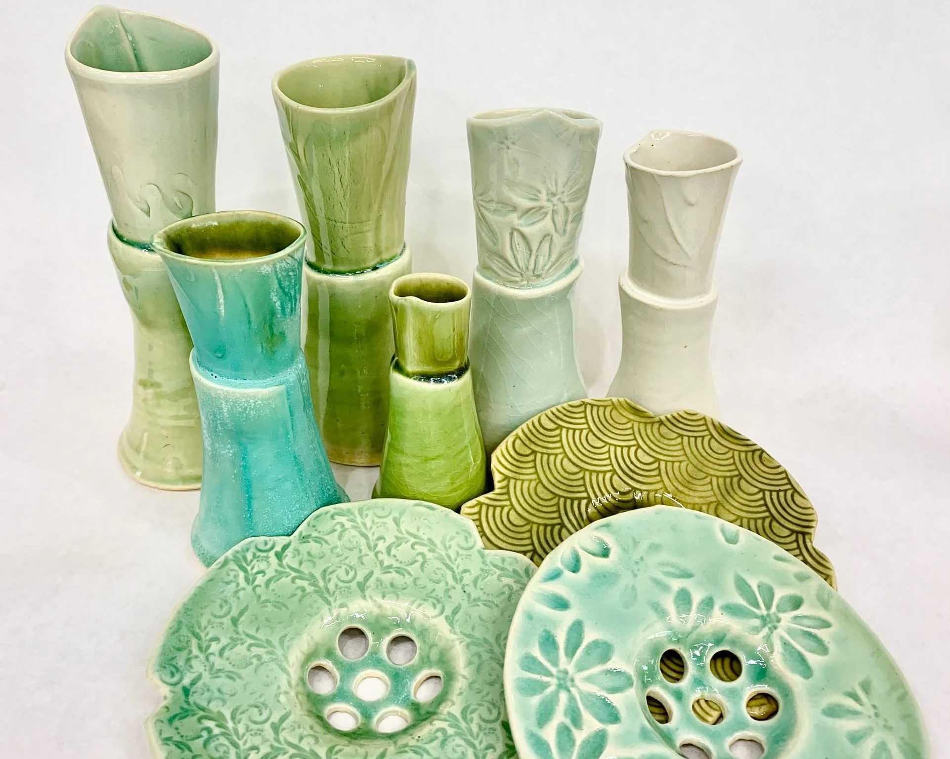 Collection of Margaret Barber's green and turquoise ceramic vases and decorative flower frogs with various patterns placed on a white background.