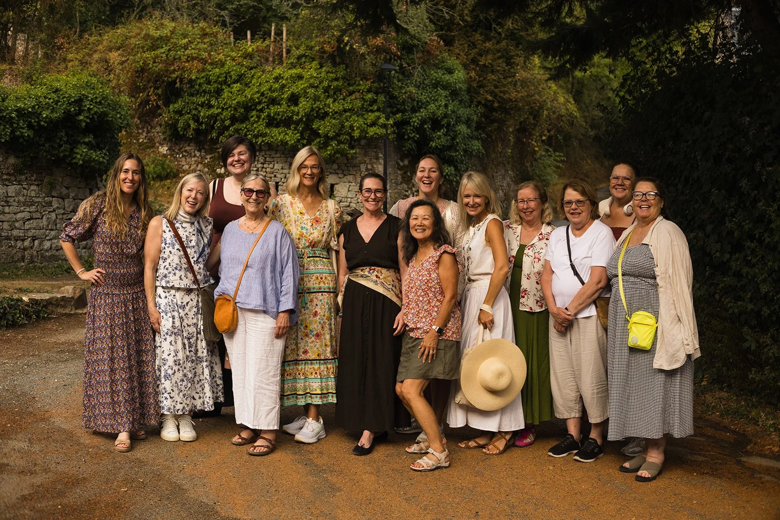 Group of women standing outdoors in front of greenery and a stone wall, smiling and posing for the photo.