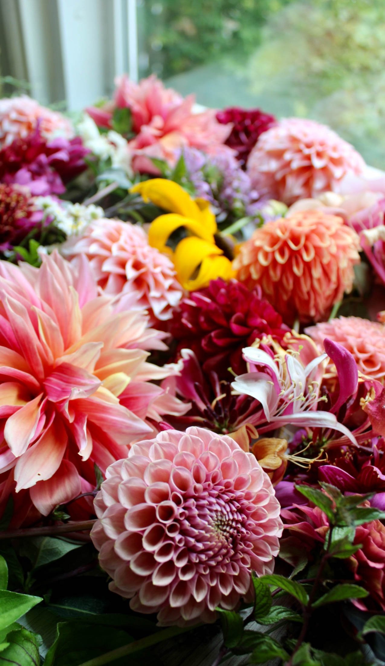Colorful bouquet of various blooming flowers, including dahlias, lilies, and other vibrant blossoms, with a blurred green outdoor background.