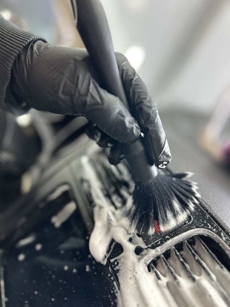 Person wearing black gloves using a brush to scrub soapy water in a car's air vent.