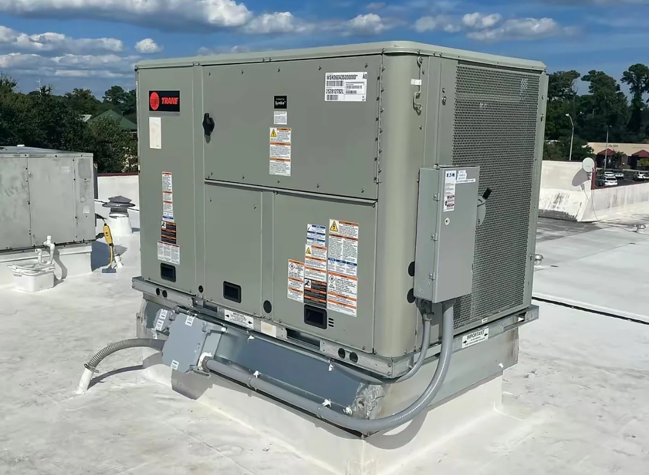 Central air conditioning unit on a rooftop with a clear blue sky and some clouds in the background.