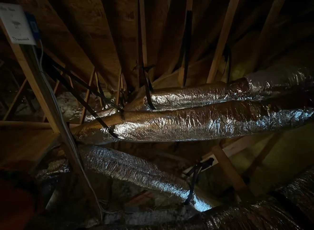 View of attic space showing wooden beams and multiple silver insulated air ducts.