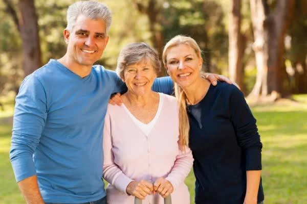 A happy family of three standing outdoors in a park, smiling and posing for a photo.