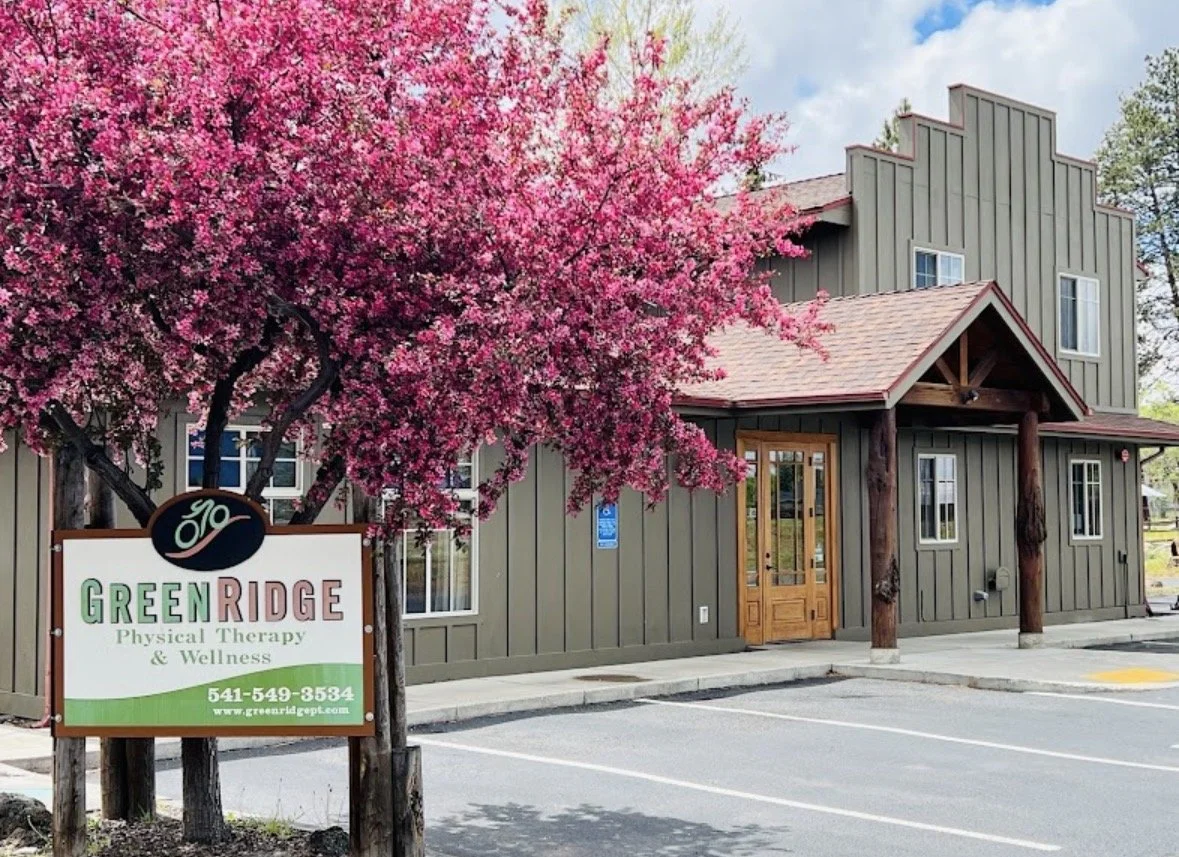 A storefront with a pink flowering tree in front, a sign for Green Ridge Physical Therapy & Wellness, and an outdoor parking lot.