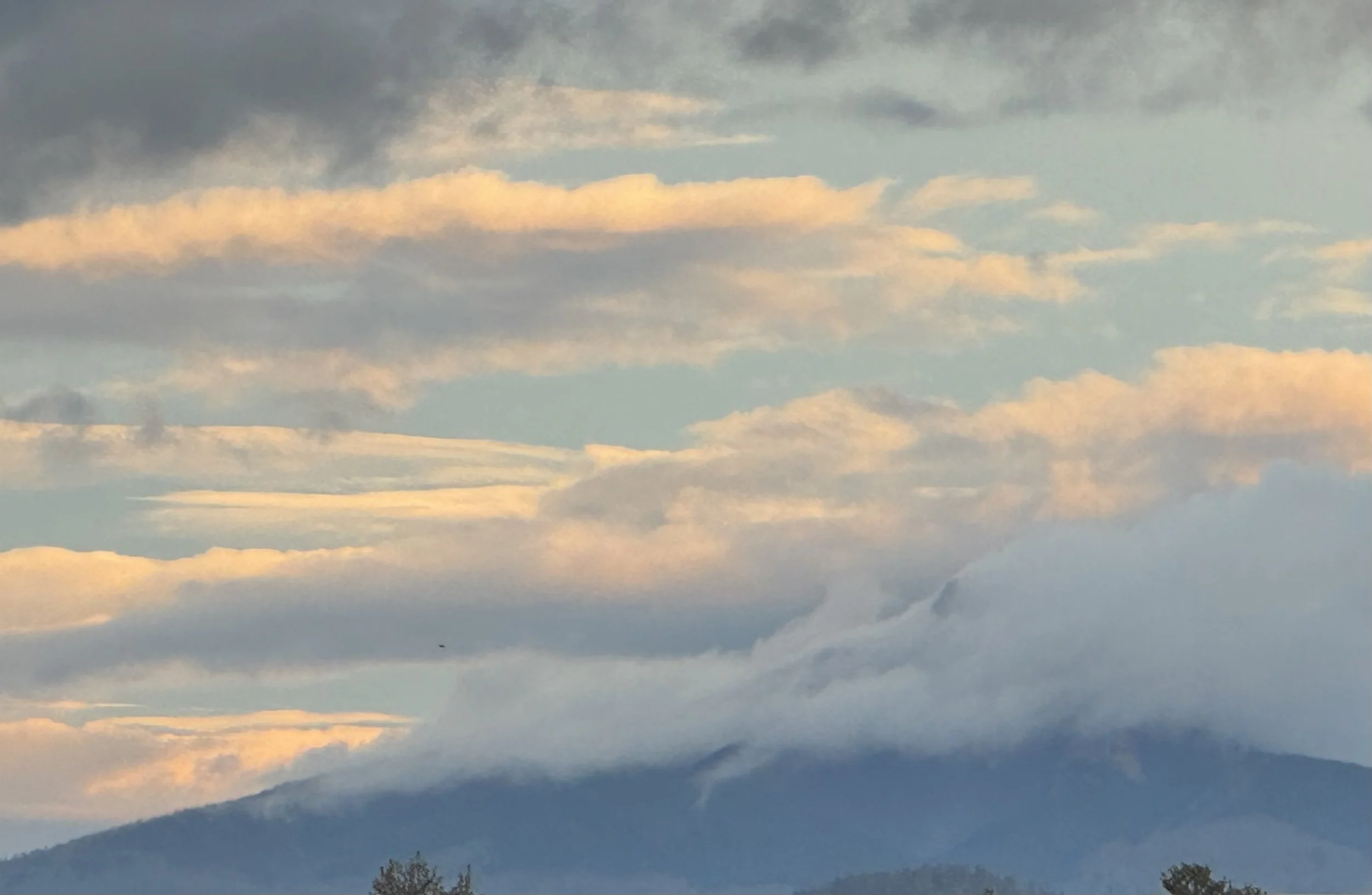 Cloudy sky over mountains at sunset or sunrise, with dark clouds and a hint of light peeking through.