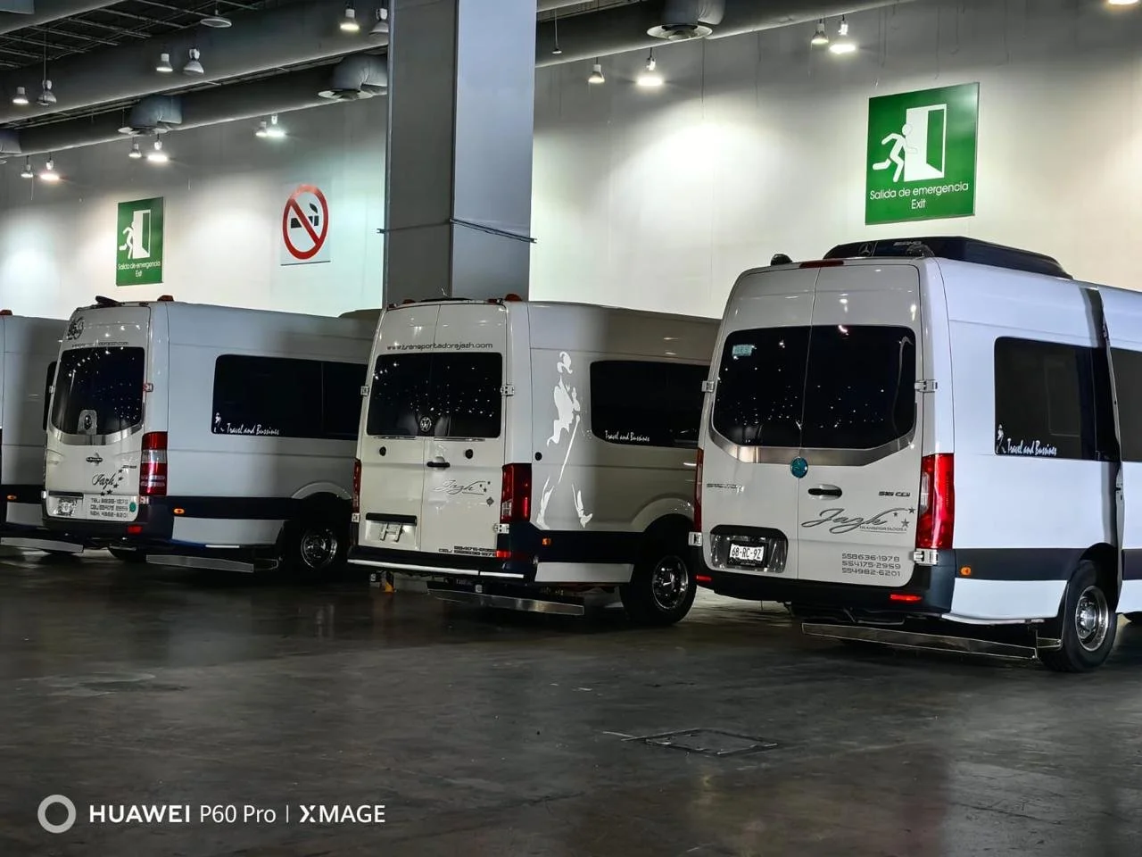 Varias furgonetas blancas estacionadas en un estacionamiento cubierto, con letreros de salida de emergencia en la pared.
