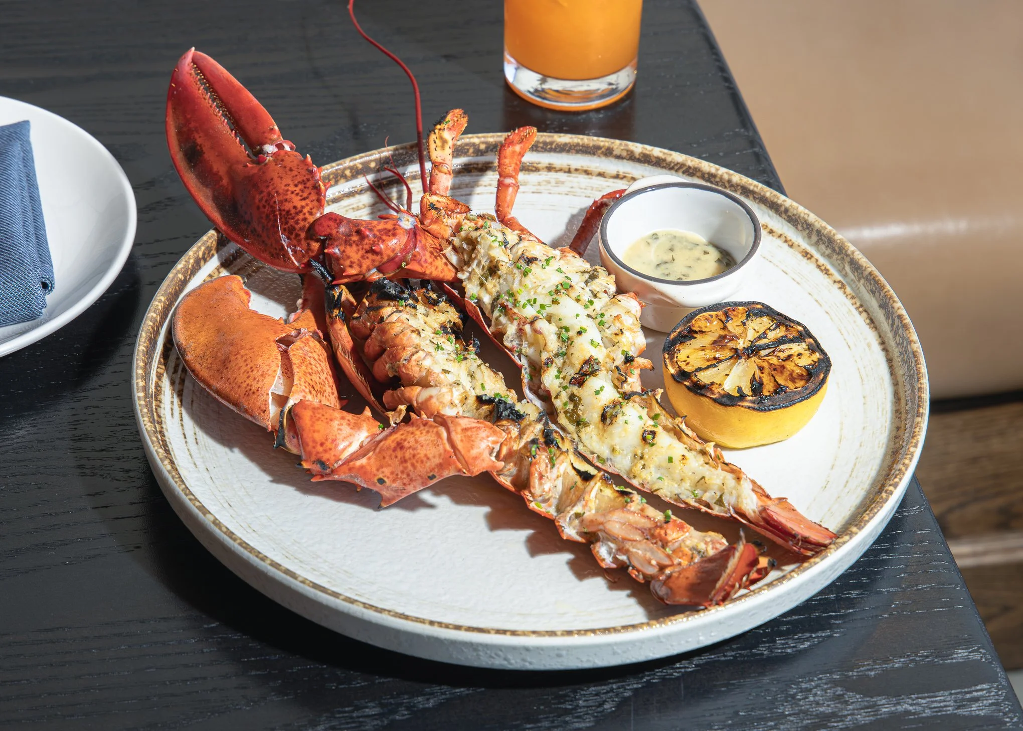 Grilled lobster served with lemon, herb butter sauce, and an orange drink
